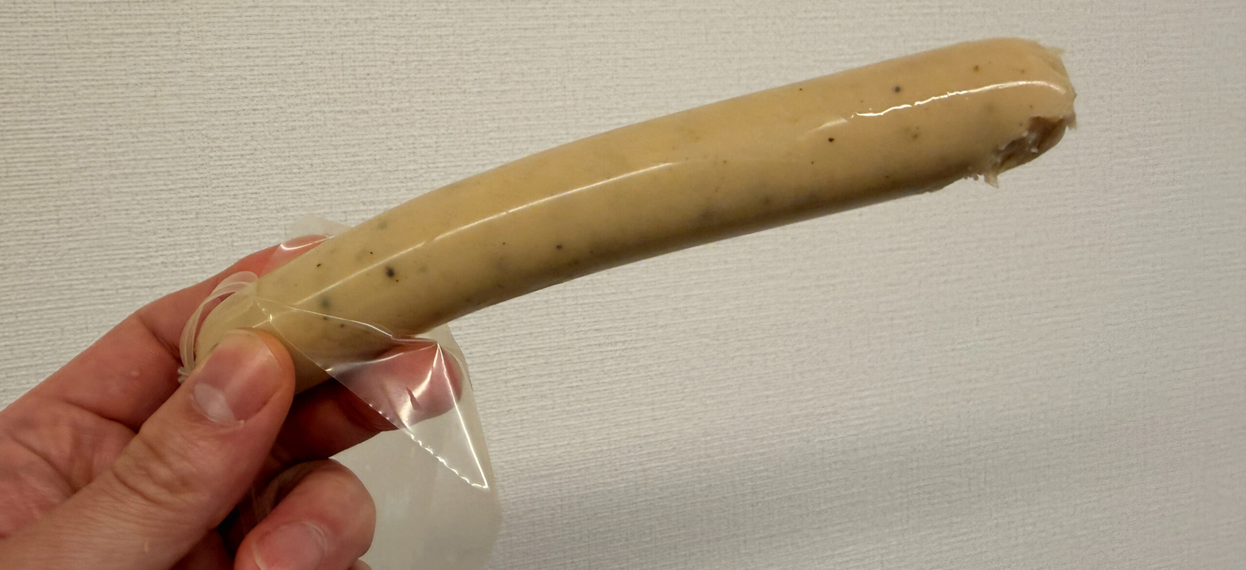 手に持たれたクリーム色のPROFITバーが透明な包装に包まれている。背景は白い壁。プレーンでシンプルな印象。