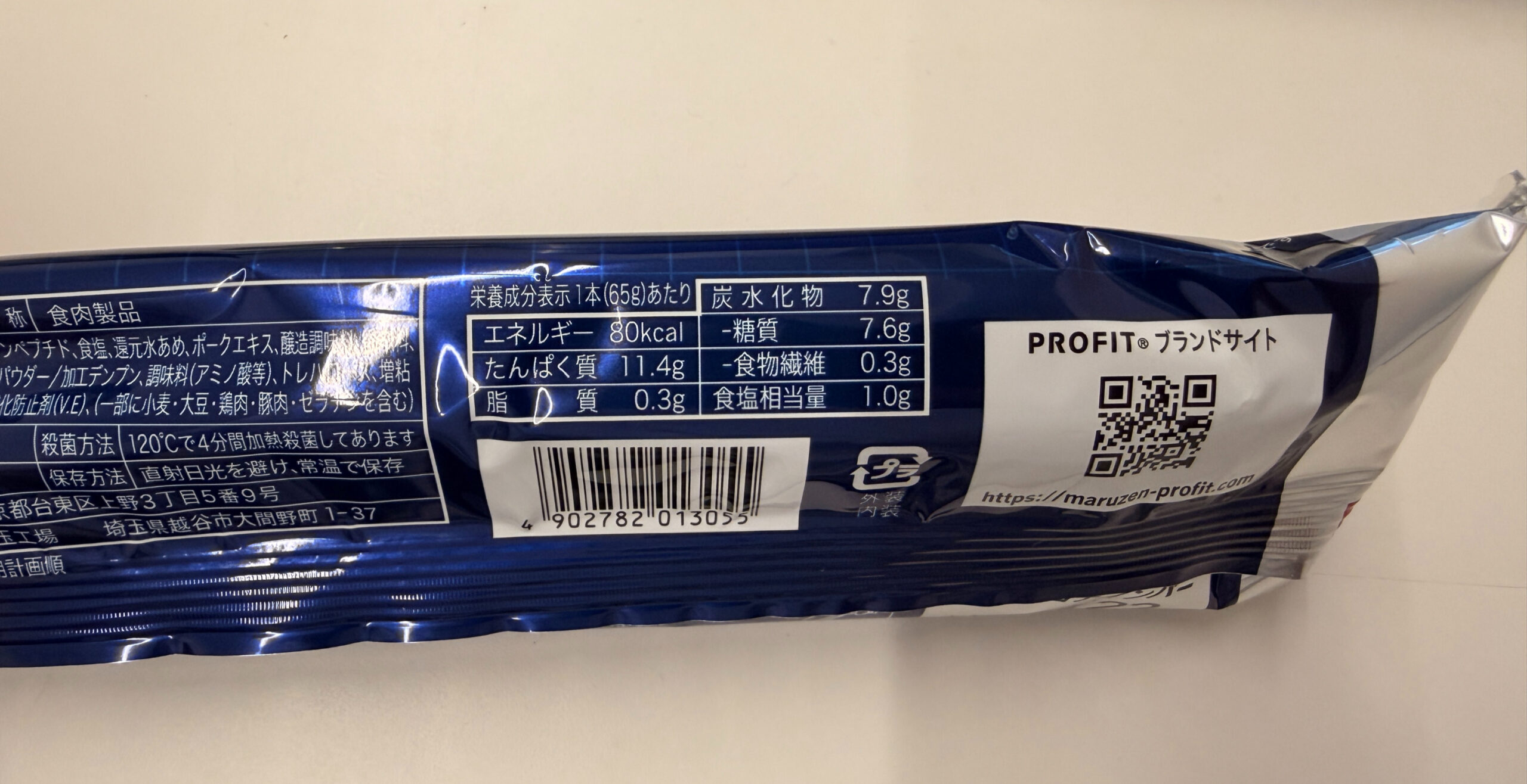 青い包装の食品パッケージがテーブルに置かれています。栄養成分表示やQRコードが印刷され、「PROFIT」ブランド名が見えます。